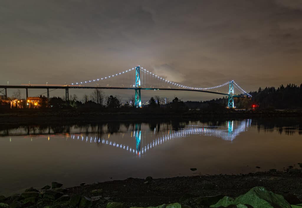 A night time photo of Lions Gate Bridge from the banks of the Capilano river in British Columbia